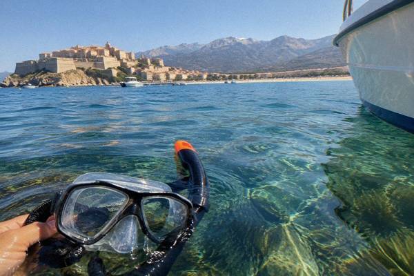 Snorkeller floating over clear water above a rocky reef near a small boat